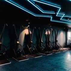 a row of exercise machines in a gym with blue lights on the ceiling and floor