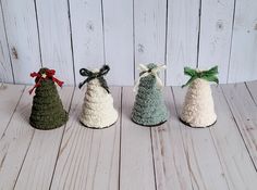 three small knitted christmas trees with bows on them sitting on a wooden table next to a white wall