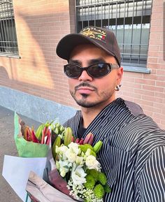 a man with sunglasses and a hat holding flowers in front of a bricked building