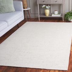 a living room area with white furniture and wood flooring, including a rug on the floor