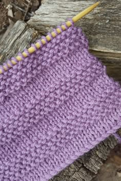 a close up of a purple knitted object on a piece of wood next to a yellow knitting needle