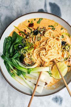 two chopsticks resting on a plate of noodles and greens