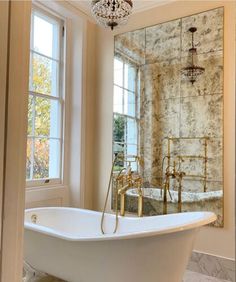 a bath tub sitting under a window next to a chandelier in a bathroom