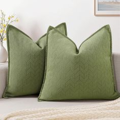 two green pillows sitting on top of a couch next to a vase with yellow flowers