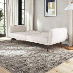 a white couch sitting on top of a wooden floor next to a lamp and window