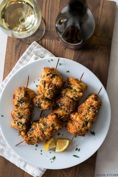 chicken skewers with lemon wedges on a plate next to a glass of wine