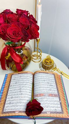 an open book sitting on top of a table next to a vase filled with red roses