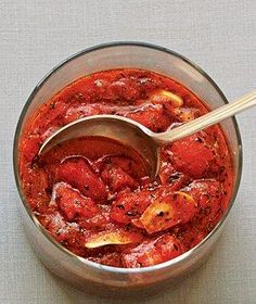 a bowl filled with red sauce on top of a white table cloth next to a wooden spoon