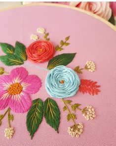 a close up of a embroidery on a pink surface with flowers in the center and green leaves