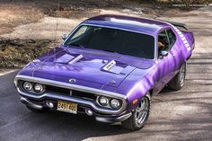 a purple muscle car parked on the side of a road next to a wooded area