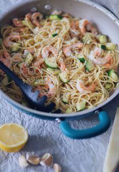 pasta with shrimp and zucchini in a skillet next to lemon wedges