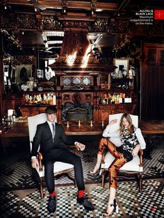 a man and woman sitting on chairs in front of a fireplace