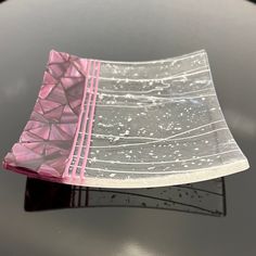 a piece of pink and clear glass sitting on top of a black table with white lines