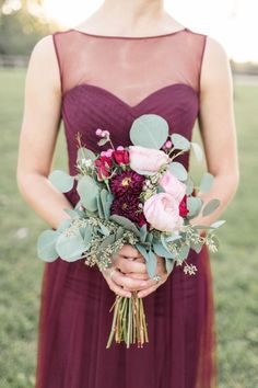 a woman in a dress holding a bouquet of flowers and greenery on her hand