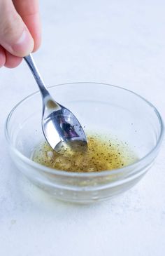 a person holding a spoon over a bowl filled with oil and seasoning mixtures