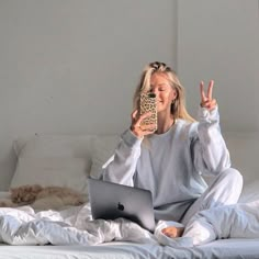 a woman sitting on a bed while holding a cell phone and looking at her laptop