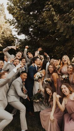 a large group of people standing around each other in front of some trees and bushes