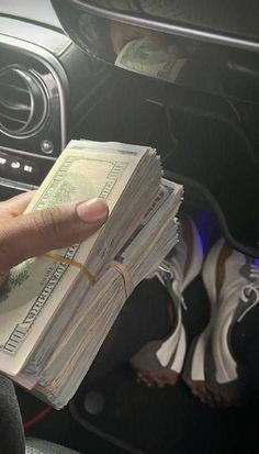 a person holding money in their hand next to a car dash board and steering wheel