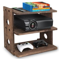 a small wooden shelf with a projector, game controller and books on top of it