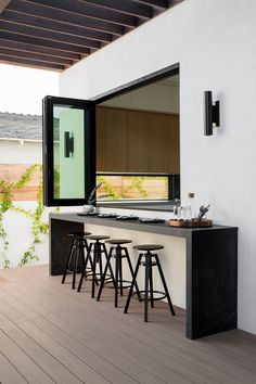 an outdoor kitchen with bar stools next to it and a large window in the back