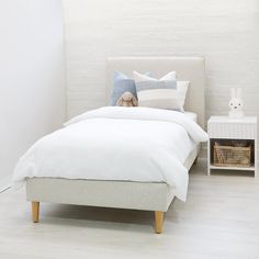 a bed with white linens and pillows in a small room next to a night stand