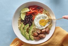 a white bowl filled with rice, meat and veggies next to a fork