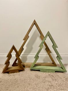 three wooden christmas trees sitting on top of a carpeted floor next to a wall