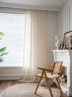 a chair sitting in front of a window next to a white fire place and potted plant