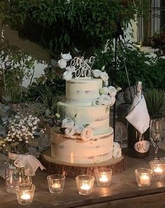 a wedding cake sitting on top of a wooden table with candles around it and flowers