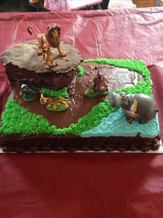 a birthday cake with animals on it sitting on a red tableclothed table cloth