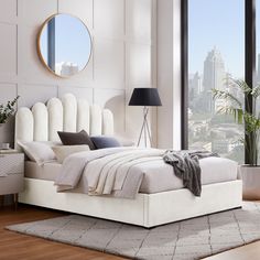 a bedroom with a large window and a white bed in the middle, surrounded by tall buildings