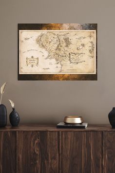 an old world map hanging on the wall above a wooden cabinet with vases and other items