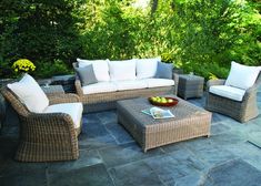 an outdoor living area with wicker furniture and stone flooring, surrounded by greenery