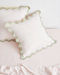 two white pillows with green scalloped edges on a pink comforter and bed