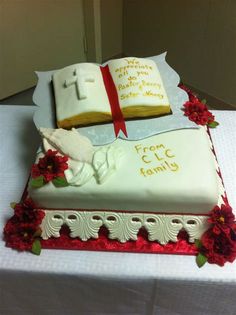 a cake decorated with an open bible and red flowers on a white tablecloth covered table