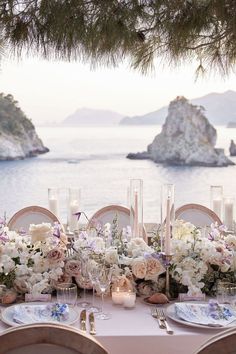 the table is set with flowers and candles for an elegant dinner by the water's edge