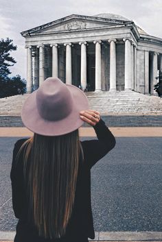 a woman wearing a hat standing in front of a building with columns on the side