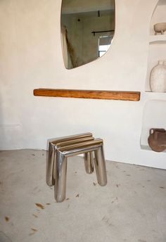 a small metal stool sitting in front of a mirror on the wall next to a shelf