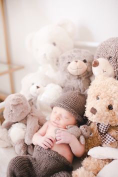 a baby is laying among stuffed animals in a pile with his hands on his chest