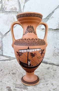 an orange vase sitting on top of a cement floor next to a stone wall with a boat painted on it