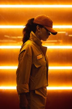 a woman wearing a baseball cap and glasses standing in front of a neon light wall