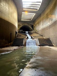 an underground tunnel with water running down the side and stairs leading up to the entrance