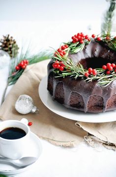 a chocolate bunt cake on a plate next to a cup of coffee and christmas decorations