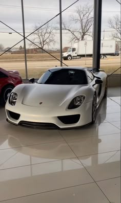 two cars are parked in a showroom with large windows and white tiles on the floor