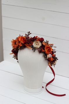 a white mannequin headpiece with orange flowers and red ribbon on the top