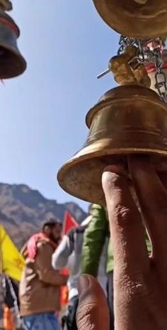 a person is holding up a bell in front of other people with flags and mountains behind them