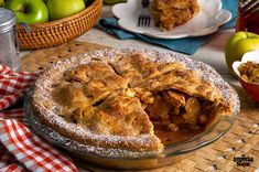 an apple pie on a table with apples in the background and a basket of apples to the side