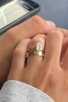 a woman's hand with two gold rings on it and a cell phone in the background