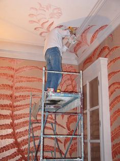 a man is painting the ceiling in an orange and white room with palm leaves on it