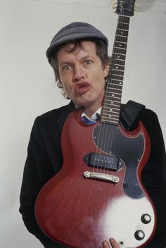 a man holding a red and black guitar in front of his face while making a funny face